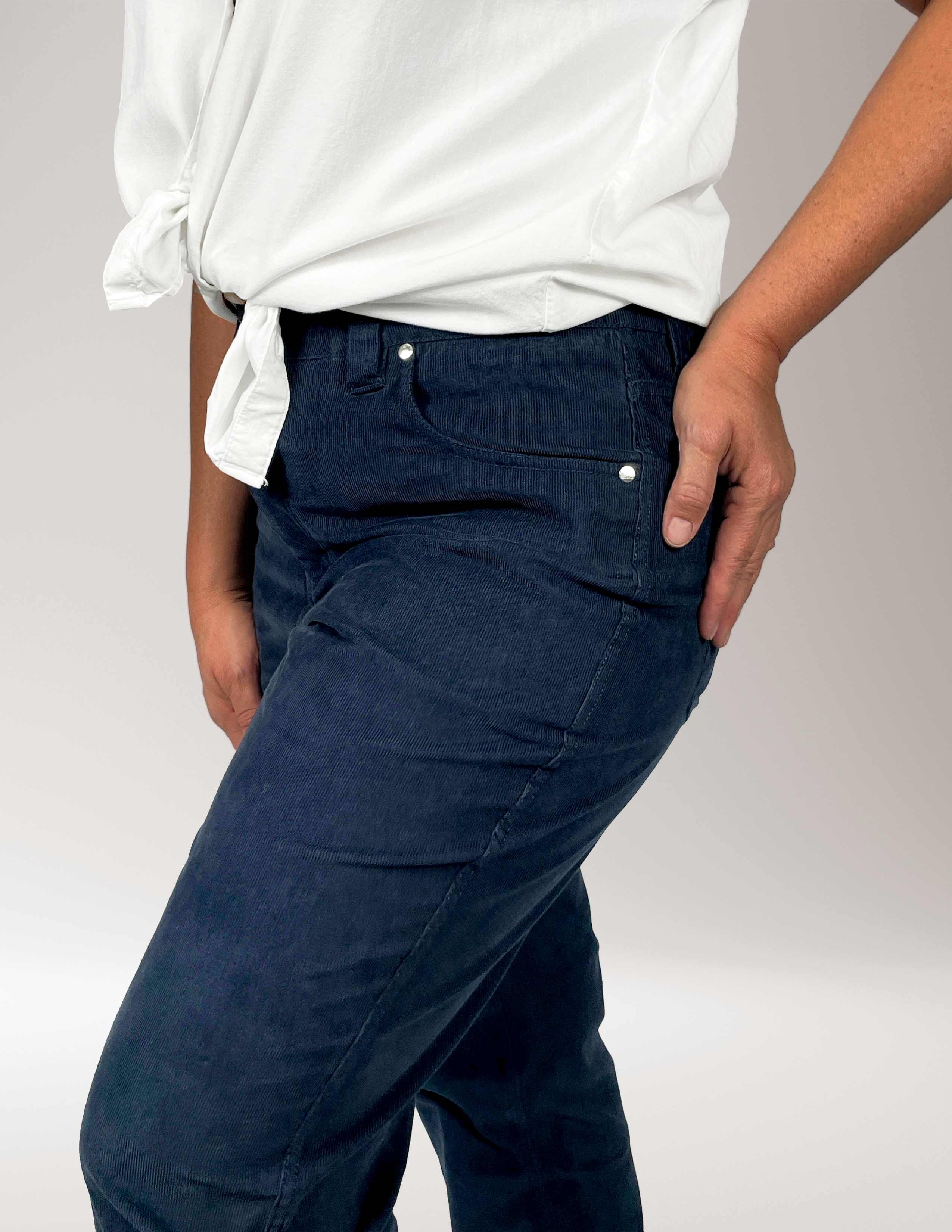 Woman wearing Cordster style pants and a white shirt on a plain background